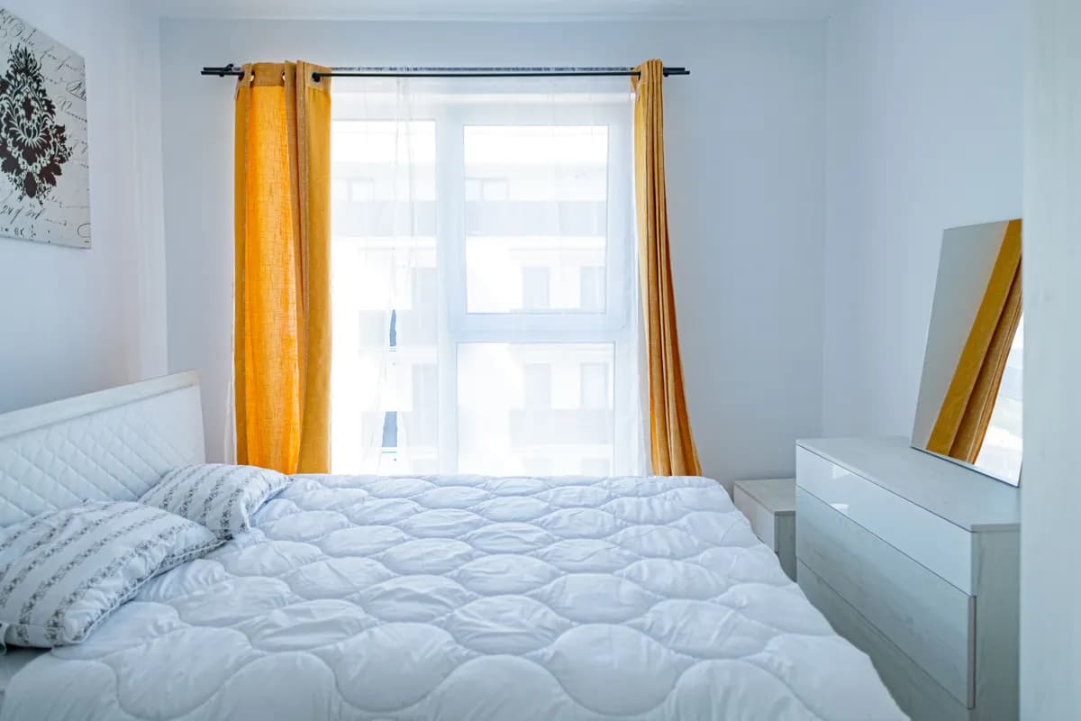 BookNoFees example image: Bedroom with a white bed and yellow curtains
