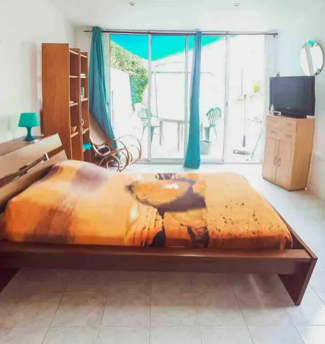 BookNoFees vacation rental in Agde, Occitania, France – Bedroom with double bed, wooden shelving unit, and sliding glass doors to patio