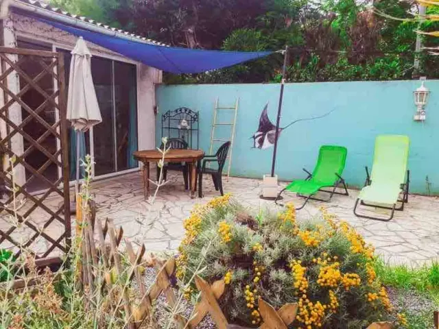 BookNoFees vacation rental in Agde, Occitania, France – Patio with stone flooring, blue shade sail, green lounge chairs, and yellow flowering plants