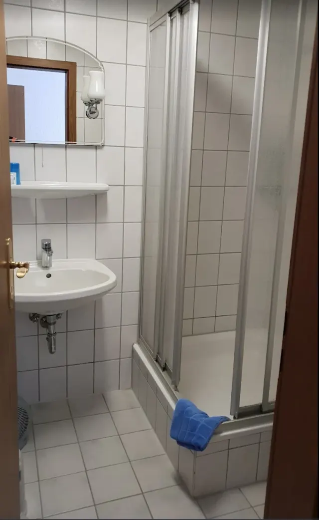 BookNoFees vacation rental in Schönfeld, Saxony, Germany – Bathroom with white sink, bathtub with shower door, and blue towel