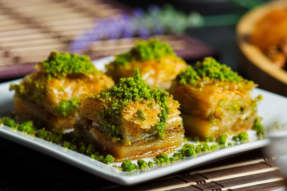 BookNoFees: Contoh foto: Empat keping baklava berlapis di atas pinggan putih, disapu kacang pistachio yang dihancurkan